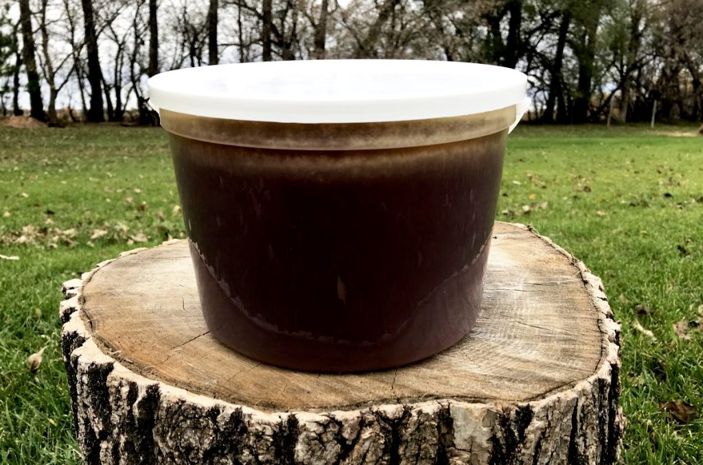 plastic pail of dark wildflower honey on a tree stump on the lawn